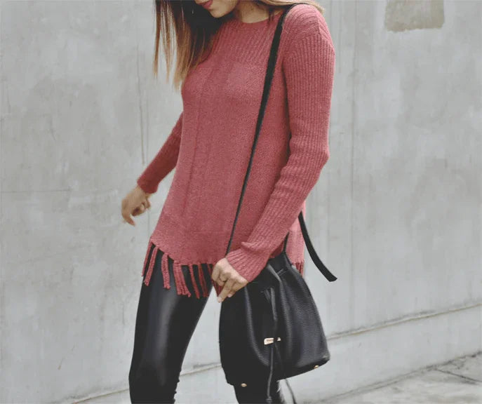 Mujer con suéter rosa de punto y flecos, pantalones negros y bolso negro de cuero