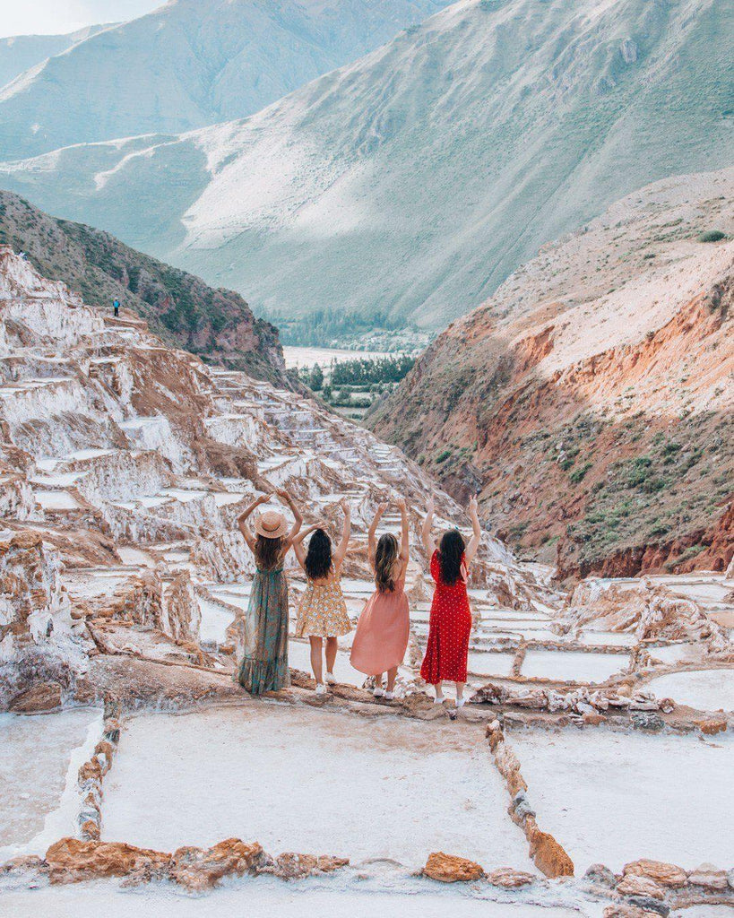 Cuatro mujeres de espaldas con vestidos coloridos en terrazas de sal en las montañas de Perú