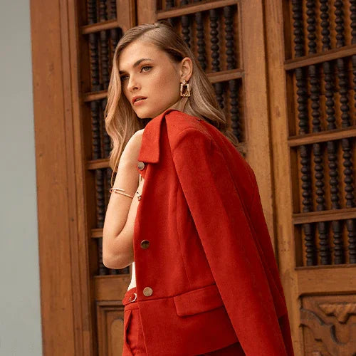 Mujer con chaqueta y pantalón rojo posando frente a puerta de madera tallada en ambiente elegante