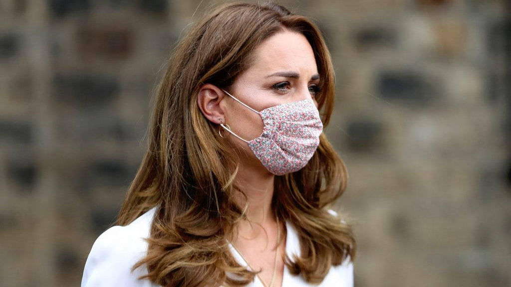 Mujer con mascarilla facial de tela rosa con estampado floral, cabello castaño suelto y chaqueta blanca