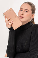 Mujer con suéter negro sostiene cartera rosa nude de piel sintética con logo MOIXX y detalles dorados