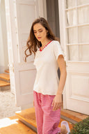 Mujer con camiseta blanca y pantalones rojos de cuadros, posando en una entrada iluminada