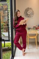 Mujer sonriente con ropa cómoda borgoña leyendo un libro junto a puerta ventana en casa moderna