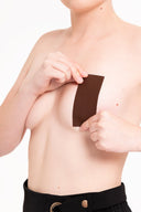 Persona aplicando parche adhesivo marrón en el pecho, fondo blanco, ropa negra