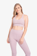 Mujer sonriente con ropa deportiva lila, top corto y leggings, fondo blanco, moda fitness