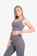 Mujer rubia con ropa deportiva gris ajustada de top y leggins con bolsillos laterales, fondo blanco