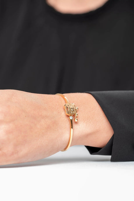 Pulsera dorada con dije decorativo en mano de mujer con manga negra, joyería elegante