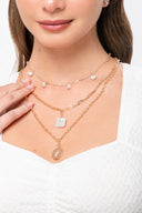 Collares dorados con dijes de perlas y medalla en cuello de mujer con blusa blanca