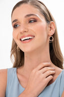 Mujer sonriente con aretes dorados de múltiples aros y vestido azul claro en fondo blanco