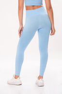 Mujer viste leggins azules ajustados y top a juego, con zapatillas blancas deportivas