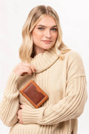 Mujer rubia con suéter beige de cuello alto sosteniendo billetera marrón MOIXX con cadena dorada