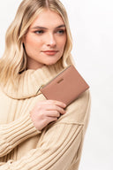 Mujer con suéter beige sosteniendo cartera rosa claro con logo Moixx y cierre dorado