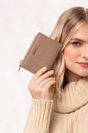 Mujer rubia con suéter beige sostiene cartera pequeña de piel marrón con logo MOIXX