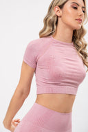 Mujer con top corto y leggins deportivos rosados, fondo blanco, enfoque en torso y perfil de rostro