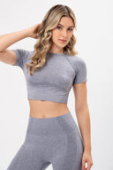 Mujer joven con ropa deportiva gris, top corto y leggings ajustados, fondo blanco